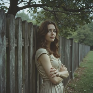 Film_19, A young woman stands serenely beside a weathered wooden fence, a slightly pensive yet hopeful expression on her face, under a leafy tree on a slightly overcast day. [Photography, photorealistic, reminiscent of 1950s/60s snapshot], [No specific artist reference, aiming for a candid, documentary style], [Shallow depth of field, focusing on the woman, slightly grainy film texture, muted natural light with slightly cool tones, Kodachrome-like color palette, background slightly blurred with a focus on the fence and tree, wet grass visible, natural setting, slightly desaturated colors for a vintage feel.