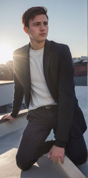 a young man sits outdoors, possibly on a rooftop, leaning forward with his arms resting on his knees. He wears a dark blazer over a white ribbed sweater, exuding a thoughtful or introspective mood. The photograph captures a soft, natural light and displays a subtle lens flare, adding an artistic touch to the serene moment.