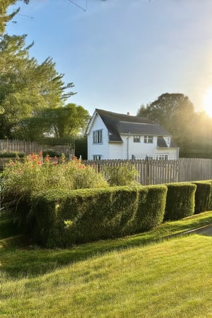 A serene morning scene: a charming white house with a lush green garden, surrounded by a rustic wooden fence. The sun shines brightly overhead, casting a warm glow on the vibrant flowers and neatly trimmed hedges. A gentle breeze rustles the leaves as the morning dew glistens on the grass.,Realistic Enhance