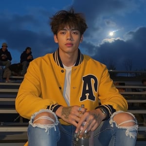 male, tall, he is muscular fit, his face is handsome with a stronger jawline,hes wearing a yellow school letter jacket, he has short kinda curly hair, he has caramel colord eyes, he is sitting the bleachers at a school football game, he has blue dennim jeans on that are ripped at the knee, he is caucasian and has a tan, and has some frekles around his nose and cheeks, he has a glass soda bottle in his hand, its in the evening so the sky is a dark blue shade and clouds blocking some of the bright moon, he has a faint stubble around his jawline and upper lip, he has a few rings on his fingers, and a few visible tattoos, there are other people sitting higher up on the bleachers,