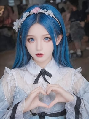 The image is a portrait of a young girl with blue hair. She is wearing a white and black dress with a black ribbon tied around her neck. The dress has a ruffled collar and sleeves. She has a small flower crown on her head with pink and white flowers. The girl is making a heart shape with her hands and is looking directly at the camera with a slight smile on her face. The background is blurred, but it appears to be an indoor space with people walking around.