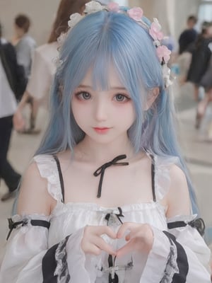 The image is a portrait of a young girl with blue hair. She is wearing a white and black dress with a black ribbon tied around her neck. The dress has a ruffled collar and sleeves. She has a small flower crown on her head with pink and white flowers. The girl is making a heart shape with her hands and is looking directly at the camera with a slight smile on her face. The background is blurred, but it appears to be an indoor space with people walking around.