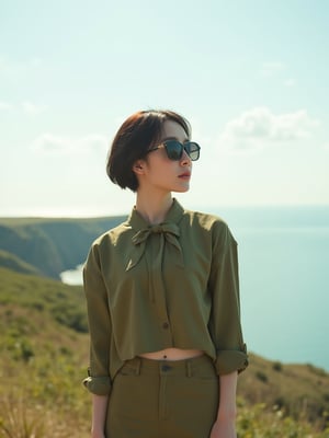 A young East Asian woman with a low fade haircut, donning a bowtie and olive green cropped shirt, skirt, and sunglasses, stands relaxed with a slight twist, gazing forward in a coastal landscape with a clear sky and lush scenery, shot in a cinematic style reminiscent of Wong Kar-wai, with soft, warm, natural light and a shallow depth of field, evoking a sense of intimacy and vulnerability, captured in a waist-up shot with a film grain texture and muted color grading.