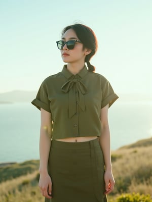 A young East Asian woman with a low fade haircut, donning a bowtie and olive green cropped shirt, skirt, and sunglasses, stands relaxed with a slight twist, gazing forward in a coastal landscape with a clear sky and lush scenery, shot in a cinematic style reminiscent of Wong Kar-wai, with soft, warm, natural light and a shallow depth of field, evoking a sense of intimacy and vulnerability, captured in a waist-up shot with a film grain texture and muted color grading.