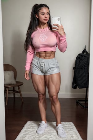 A heavily muscled iffb pro female bodybuilder,  Full-body mirror selfie of a muscular woman standing in a room with a wooden floor. She has long, dark hair with pink highlights and is wearing a black long-sleeve top and light green shorts. She is holding a smartphone with a reflective case in her left hand. She is also wearing white and gray athletic shoes with white socks. The room has a white wall with a calendar or planner hanging on it, and there is a black and white patterned rug on the floor. In the background, there is a black bag and some other items partially visible.