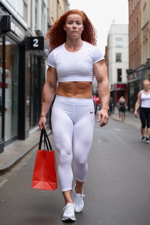 A heavily muscled female crossfit athletic, 
 red headed, ginger hair,  wearing a white t-shirt. BREAK black leggings. BREAK white sneakers,  she is walking along the highstreet in an English city , there are other people walking and shopping 