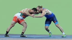 A dynamic, close-up shot of two Greco-Roman wrestlers, their chiseled bodies glistening in the warm light of a sun-drenched arena. Their faces, determined and focused, are bent towards the mat as they wrestle nude, hands grasping for each other's arms and bare feet tangling in a fierce struggle.