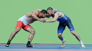 A dynamic, close-up shot of two Greco-Roman wrestlers, their chiseled bodies glistening in the warm light of a sun-drenched arena. Their faces, determined and focused, are bent towards the mat as they wrestle nude, hands grasping for each other's arms and bare feet tangling in a fierce struggle.