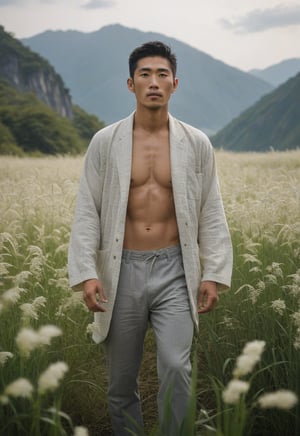 A serene 29-year-old Japanese man stands tall amidst a field of Imperata cylindrica with delicate white flowers swaying gently in the breeze. His luminous complexion radiates a subtle sheen as he poses dynamically against the majestic mountains shrouded in misty serenity. The dampened attire clings to his toned physique, emphasizing the harmonious golden ratio composition.