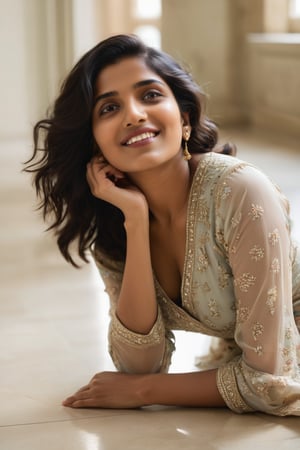 A young Indian woman lies down on a neutral-colored floor, her modern dress subtly torn to reveal a glimpse of skin as she smizes at the camera. Her beautiful face is tilted upwards, making gentle eye contact with the viewer from a low-angle perspective. One leg is bent and lifted, with about one-third of it exposed in a playful pose, inviting the audience into her intimate space.