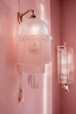 in style of Rene Lalique,Bedroom White lamp,modern style,new Chinese style,Mottled light shadow,Warming lighting,photography,Telephoto lens,Bauhaus,Placed in a corner of a girl's pink bedroom,Details show lotus pattern,Thin and transparent, shaped like a lotus,Modernism,elegant,warm,tassel