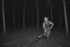 A crippled boy walks through the woods with an axe looking for her father to slay them, his mad face scares anyone who meets him, he is running to hunt the viewer.,monochrome