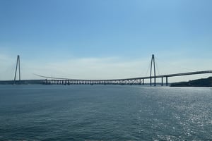 A scenic shot of the iconic Penang Bridge, stretching 13.5 kilometers across the water, connecting the island of Penang to the mainland. The late afternoon sunlight casts a warm glow on the sleek steel structure, while the surrounding waters sparkle like diamonds. A slight haze hangs in the air, adding depth to the composition. The bridge's gentle curves and rhythmic arches create a sense of dynamism, as if it's about to spring into motion.