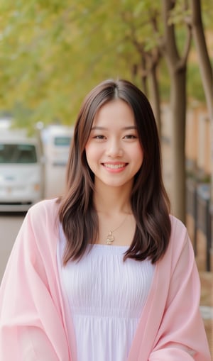 a young Asian woman with long brown hair, wearing a white dress with a pink shawl draped over her shoulders. She is smiling, her lips are slightly parted, and her eyes are slightly open. She's wearing a gold necklace with a pendant hanging from it, adding a touch of charm to her outfit. In the background, a row of trees, their leaves changing color from yellow to green, are visible. To the left of her, a white van is parked on the street.