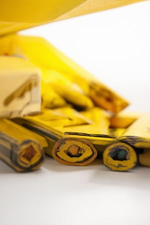 A close-up shot of a bright yellow crayon box against a plain white background, with softbox lighting to highlight its vibrant hue. The box is centered in the frame, surrounded by a shallow depth of field to blur the background and emphasize the warm color. A few loose crayons are scattered around the box, adding texture and visual interest.