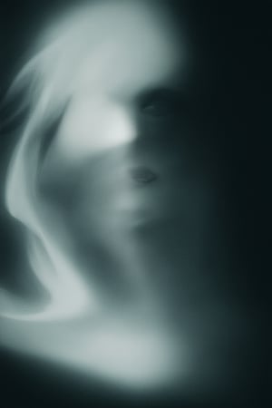 A moody portrait of a person shrouded in darkness, with only a faint glow illuminating their features. The subject's face is obscured by shadows, with only hints of their facial structure visible. The darkness is so profound that it seems to take on a life of its own, swirling around the figure like a palpable entity.