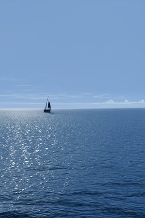 A dreamy, ethereal seascape: a serene Deep Blue ocean stretches out before us, its gentle waves lapping at the shore. Soft sunlight filters through wispy clouds, casting an otherworldly glow on the water's surface. A solitary sailboat drifts lazily across the frame, its billowing sails and slender mast creating a sense of tranquility.