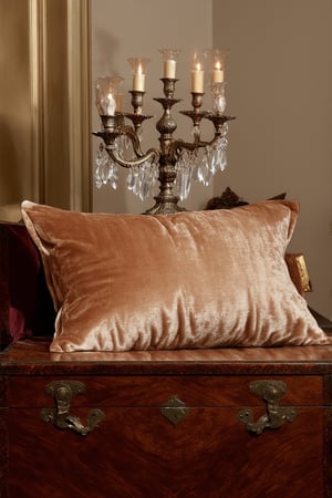 A sumptuous still life captures the essence of luxury: a velvet-soft pillow rests against a richly textured antique wooden chest, adorned with intricate carvings and a subtle patina. A delicate silver candelabra stands tall, its multiple arms holding ornate crystal holders that refract warm golden light. Soft focus highlights the plush texture of the pillow and the aged wood grain, inviting the viewer to touch and experience the opulence.