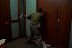 35mm film stock, 50mm f16 lens. Still image from a 1972 psychological horror film. The inside of a large manager's office. 
We are facing our hero, 25 years old, brown hair, wearing charcoal slacks, a skinny tie, and an olive drab combat fatigue jacket. He is breaking down the walnut door to the Villian's office with a fire axe.
Filmed from the ground looking up, dramatic lighting, subtle blue-green cast fluorescent lighting.,deep focus style,Technicolor style