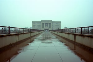 35mm Fuji Velvia film stock, 50mm f16 lens. An empty cement civilian walkway in the middle of a dystopian city. A Soviet-style Brutalist building stands before us, a building of nonesense. The sky is a neutral gauzy gray.,RonFricke cinematic film style. Light drizzling rain. Depressing