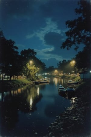 A 1990s nighttime view of a river in Malaysia, with the scene bathed in soft, ambient lighting from nearby street lamps and the moon. The river is calm, reflecting the dim glow of the lights and the starry sky. The banks are lined with trees and bushes, casting long shadows. A few boats are moored along the shore, their silhouettes barely visible in the low light. The atmosphere is peaceful and tranquil, capturing the essence of a 1990s Malaysian night by the river.