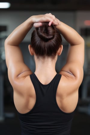 Captured at eye-level, a medium-angle shot of a woman in a gym poses with her arms stretched out in front of her. Her hair is pulled back in a bun, cascading over her shoulders and cascading down her shoulders. She is wearing a black tank top and black leggings, and black sneakers. Her nails are painted with black nail polish, adding a touch of color to her outfit. The background is blurred, suggesting a gym setting.