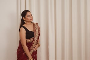 a medium-sized sexy indian woman stands in sidewise in front of a white curtain. She is dressed in a black sleeveless blouse with a maroon sari adorned with gold embroidery. Her hair is pulled back in a ponytail, and she is adorned with a pair of dangling earrings. Her bangles are gold, adding a touch of contrast to her dress. The backdrop is a stark white, creating a stark contrast to the woman's outfit.,photorealistic,Anupama, Warm Lighting,TamannaFlux, IMG0095.HEIC