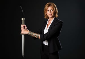 Create an image of Dana Scully standing confidently, wielding the Witchblade on her right wrist and forearm. She should be dressed in a fitted, stylish FBI attire that subtly accentuates her figure, such as an open tailored blazer, over a sleek blouse with the top button undon. Her expression is one of empowerment and determination, showcasing her strength. The Witchblade should appear as a grey, intricate artifact with jewels, wrapping around her forearm up to her elbow and radiating energy, enhancing her commanding presence.  A sharp blade protrudes from the top of her wrist.  The background hints at a dark and mysterious atmosphere, with shadows of supernatural elements, emphasizing her dual role as a fierce investigator and a powerful wielder of the Witchblade. The image should capture a sense of allure without compromising Scully's integrity, reflecting her as a formidable and sexy force in the realm of the supernatural.