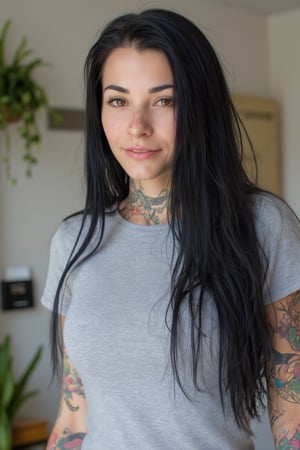 Close-up photograph of a 30yo Su1c1de_G1rls woman with very long black hair falling down over her shoulders. The woman has a cute round face with freckles and smiles. The woman is wearing a skin-tight fitted light Grey t-shirt with short sleeves made from smooth stretch fabric. There are many colored tattoos of dragons and flowers on her arms, neck and collarbone. She is standing in an apartment with plants and book shelves.