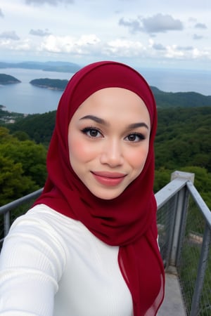 This is a high-resolution photograph featuring a young woman taking a selfie at an elevated viewpoint, likely a lookout or skywalk. The woman is of South Asian descent, with fair skin and a round face adorned with meticulously applied makeup, including bold, winged eyeliner and matte lipstick in a deep red shade. She wears a white, long-sleeve ribbed knit sweater ((extra tight)) and a voluminous, rich red hijab that flows gracefully around her, covering her head and shoulders. 

Her hijab is made of a lightweight, sheer fabric that allows for a soft, delicate texture contrasted against the knit sweater. She has a confident smile and is looking directly at the camera, capturing the moment with her right arm extended.

In the background, the scene extends to a breathtaking panoramic view of lush green forested hills and a vast body of water, likely a sea or lake, under a partly cloudy sky. The horizon is distant, with faint outlines of distant islands and the coastline. The overall mood of the image is serene and picturesque, highlighting both the beauty of nature and the woman's elegant attire.