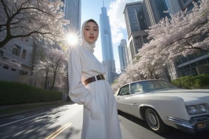 A high-angle, ultra-wide shot frames an Asian hijab woman's captivating portrait, illuminated by a strobe light's sharp, high-contrast glow. She poses with effortless elegance in trendy, all-white attire with belt and accessories, against a backdrop of lush sakura trees and a cityscape dominated by a skyscraper. The street below is bathed in the soft, gradient shadow of the building, while a sleek, white classic car beside her adds a touch of sophistication.