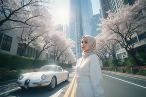 A high-angle, ultra-wide shot frames an Asian hijab woman's captivating portrait, illuminated by a strobe light's sharp, high-contrast glow. She poses with effortless elegance in trendy, all-white attire with belt and accessories, against a backdrop of lush sakura trees and a cityscape dominated by a skyscraper. The street below is bathed in the soft, gradient shadow of the building, while a sleek, white classic car beside her adds a touch of sophistication.