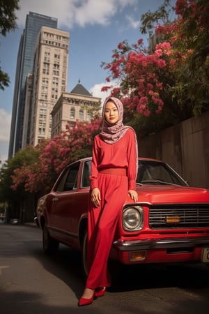 A striking low-angel shot captures an Asian hijab woman's mesmerizing portrait, warmly lit by a strobe light casting sharp shadows. Her long scarf flows gently in the breeze as she poses effortlessly in all-red-pink attire with matching accessories against a vibrant backdrop of red flower trees and city skyscrapers. The street below is bathed in soft gradient shadow, while a sleek classic red car beside her adds sophistication.