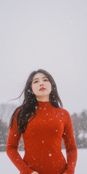 A young woman stands under a blanket of snowflakes gently falling from the gray winter sky. She wears a tight-fitting red dress, her long hair blowing in the gentle breeze as she gazes upwards, lost in thought. The camera frames her from the waist up, with the snowy landscape blurred behind her.,Film Photography