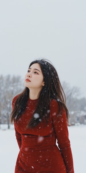 A young woman stands under a blanket of snowflakes gently falling from the gray winter sky. She wears a tight-fitting red dress, her long hair blowing in the gentle breeze as she gazes upwards, lost in thought. The camera frames her from the waist up, with the snowy landscape blurred behind her.,Film Photography