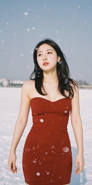 A young woman stands under a blanket of snowflakes gently falling from the gray winter sky. She wears a tight-fitting red dress, her long hair blowing in the gentle breeze as she gazes upwards, lost in thought. The camera frames her from the waist up, with the snowy landscape blurred behind her.,Film Photography