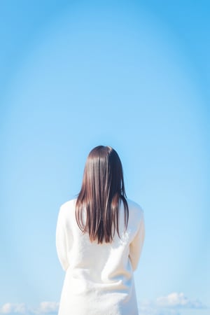 An extra long shot landscape photo showing a young Asian woman standing in front of blue sky. The woman has long hair, wears white sweater dress. The overall image shows a minimalistic and dreamini style.