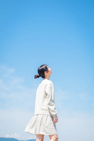 An extra long shot landscape photo showing a young Asian woman standing in front of blue sky. The woman wears white sweater dress. The overall image shows a minimalistic and dreamini style.