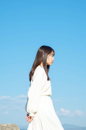 An extra long shot landscape photo showing the profile of a young Asian woman standing in front of blue sky. The woman has long hair, wears white sweater dress. The overall image shows a minimalistic and dreamini style.