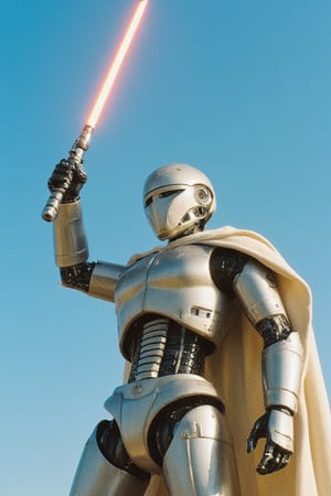 A robot stands heroically, clad in a worn Jedi robe and grasping a gleaming lightsaber. The midday sun casts a warm glow, illuminating the metallic sheen of its body as it holds the blade aloft, ready to defend against an incoming attack. Framed against a bright blue sky, the robot's pose exudes strength and determination.