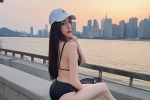 young woman sitting on a concrete wall by the water. She is wearing a black bikini and a white baseball cap. The woman has shoulder-length dark hair and is looking directly at the camera with a serious expression. In the background, there is a city skyline with tall buildings and a body of water. The sky is orange and pink, indicating that it is either sunrise or sunset. The overall mood of the image is peaceful and serene,txznasian7