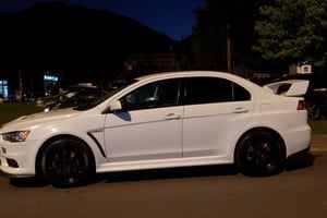 photo of Mitshubishi lancer evolution 10,shiny white paint, black rims, parked on the side of the road, photo taken at night with a cellphone flash