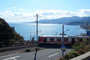 photo of a train crossing on the Kamakura road in Japan with a view of blue sea water and reflected sunlight, photo taken with a super realistic quality cell phone