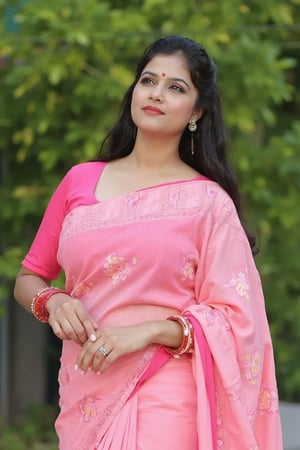 A very beautiful indian woman poses gracefully outdoors, wearing a pink saree with floral patterns that drapes elegantly over her body. She has a fitted pink blouse with three-quarter sleeves and a decorative bindi on her forehead. Her long, dark hair falls softly over her shoulders, and her gaze is directed upward with an expression of confidence. Red bangles adorn her wrists, adding a touch of traditional elegance to her look. The background features blurred greenery, suggesting a natural setting.