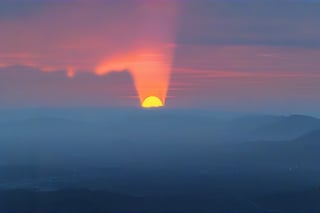 a dense layer of gray clouds illuminated in light rose color from above, a small golden sun, light gray mountains in the distance on the horizon among which power plants and industrial buildings can be seen, closer gray mountains on the horizon among which power plants and industrial buildings can be seen, black mountains on the horizon among which power plants and industrial buildings can be seen,