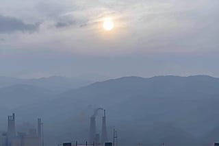 a dense layer of gray clouds illuminated in light rose color from above, a small golden sun, light gray mountains in the distance on the horizon among which power plants and industrial buildings can be seen, closer gray mountains on the horizon among which power plants and industrial buildings can be seen, black mountains on the horizon among which power plants and industrial buildings can be seen,