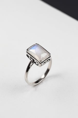 A silver ring with a delicate rectangular moonstone, with a white background on a black box