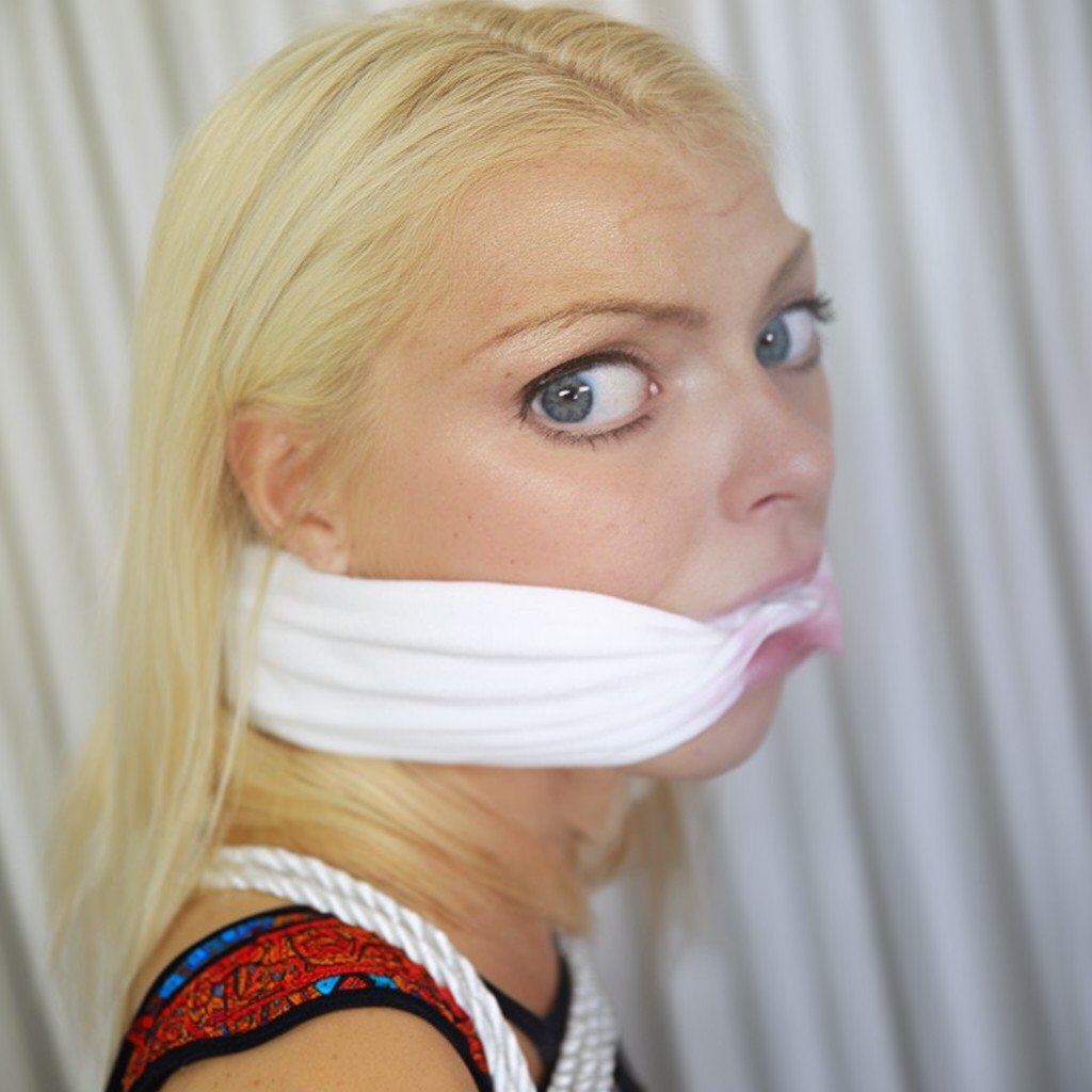 A close-up,  eye-level portrait captures a blonde woman with striking blue eyes looking directly into the lens. Her expres...