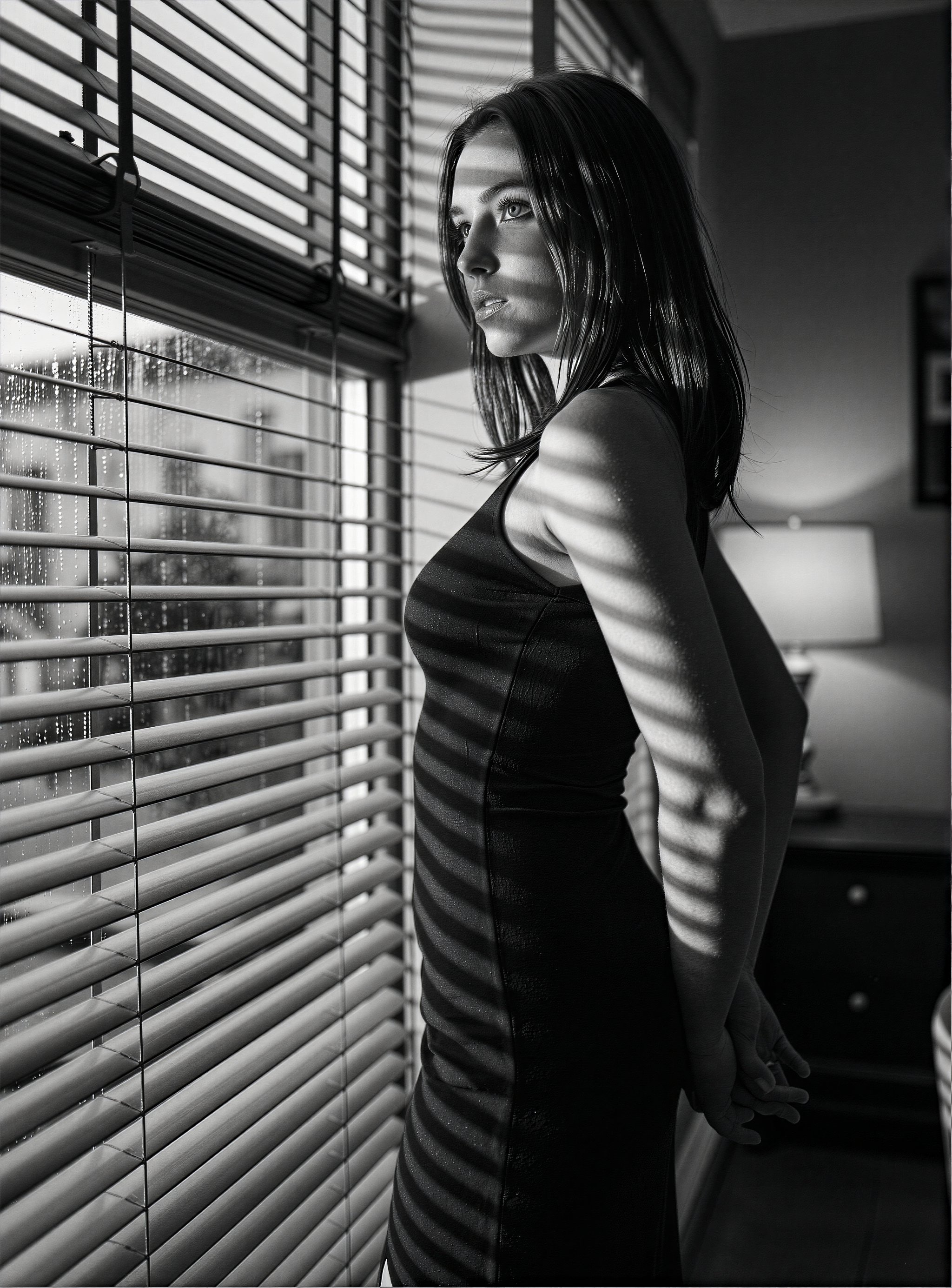 A tall,  poised adult woman in her late 20s stands upright by a tall window,  her slim figure framed in a sharp by psychol...