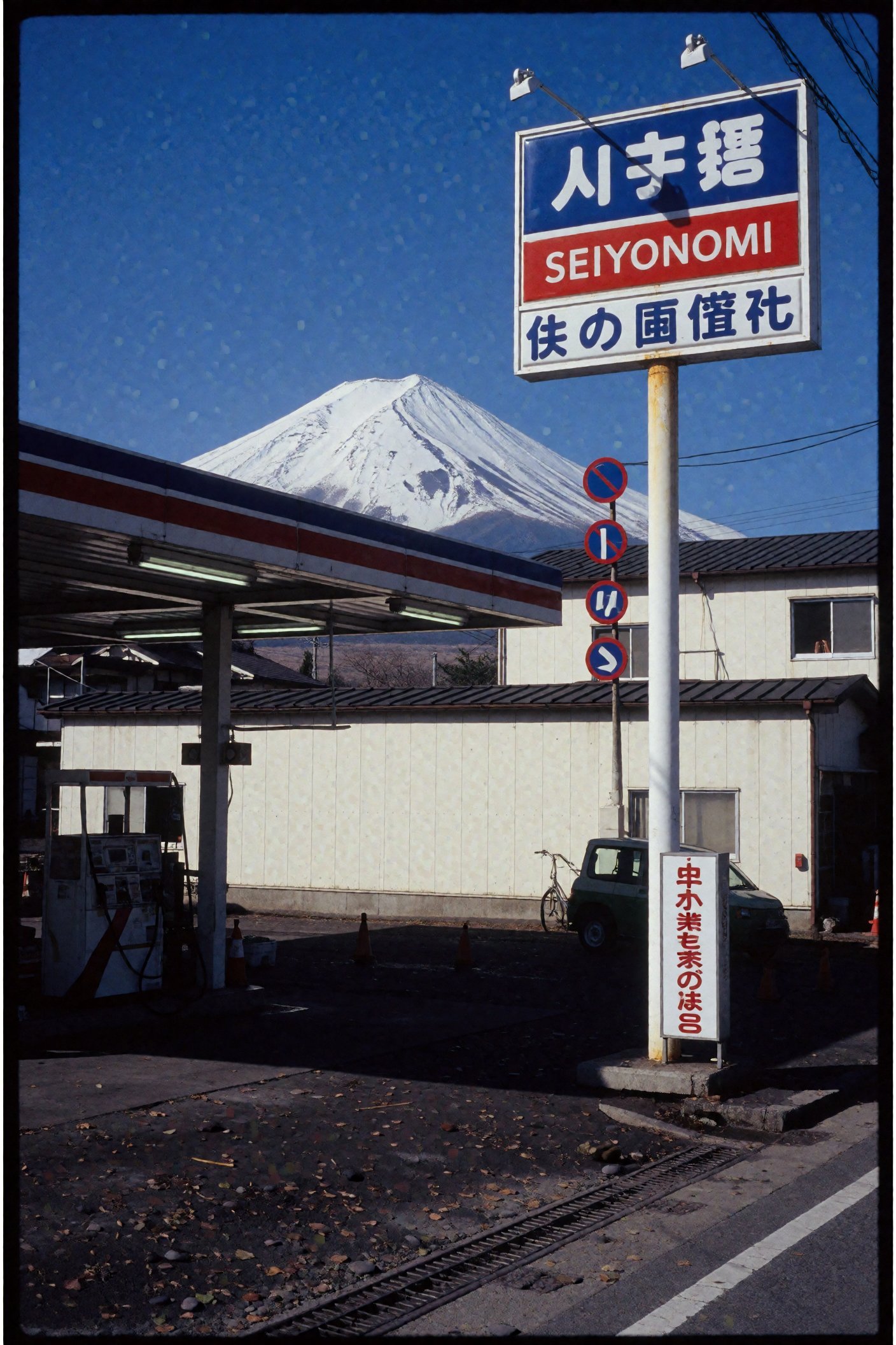 Photograph of a small Japanese gas station with a blue,  red,  and white sign reading "SEIYONOMI" in Japanese characters....